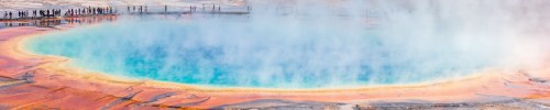 A vibrant geothermal hot spring with blue water and colorful mineral deposits, surrounded by steam and visitors in the background.