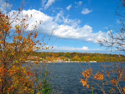 A serene lake scene with autumn foliage and a blue sky filled with clouds.