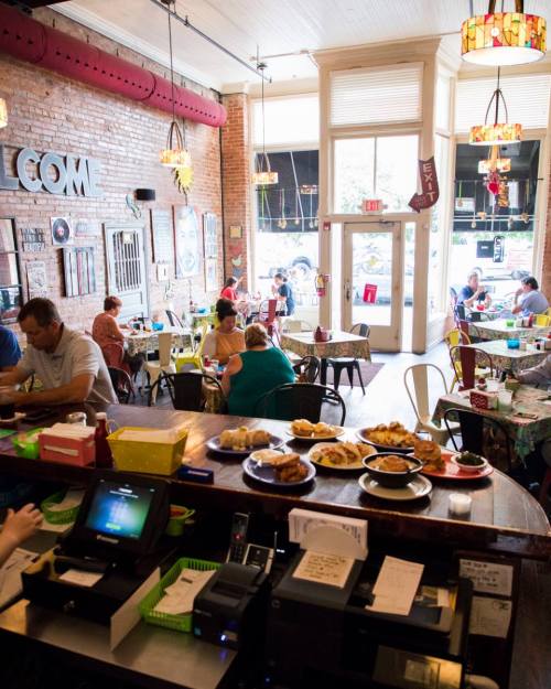 A cozy café interior with patrons dining, colorful decor, and a counter displaying pastries and a cash register.