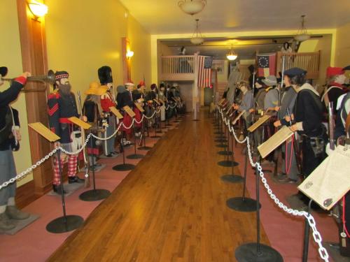 A museum hallway lined with historical mannequins in various military uniforms, with flags and informational plaques.