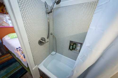 A modern shower with a hexagonal tile design, featuring a handheld showerhead and a white curtain.