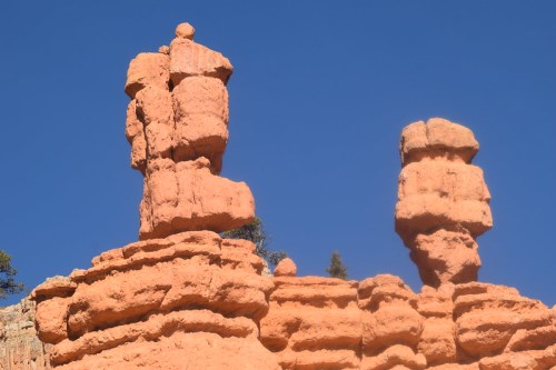 Two tall, reddish rock formations stand against a clear blue sky, showcasing unique natural shapes.