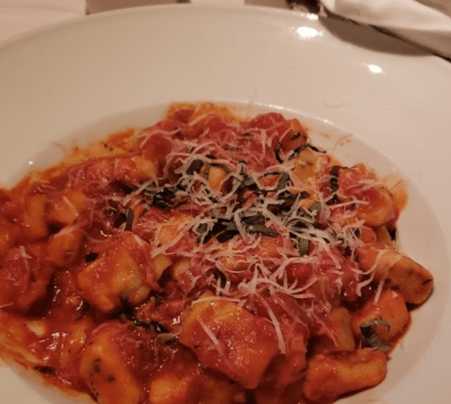 A plate of gnocchi in a rich tomato sauce, topped with shredded cheese and fresh basil.