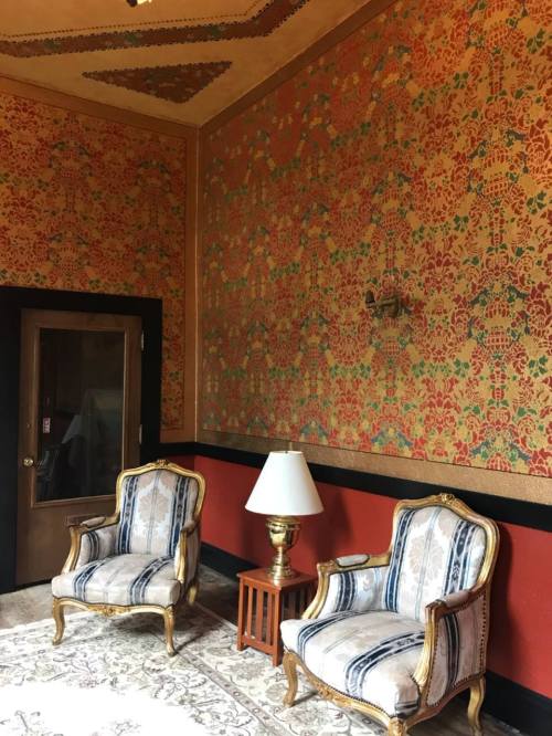 A cozy room featuring two ornate chairs, a lamp, and vibrant patterned wallpaper.