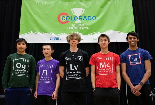 Five students stand in front of a banner for the Colorado High School Science Bowl, wearing themed T-shirts with element symbols.