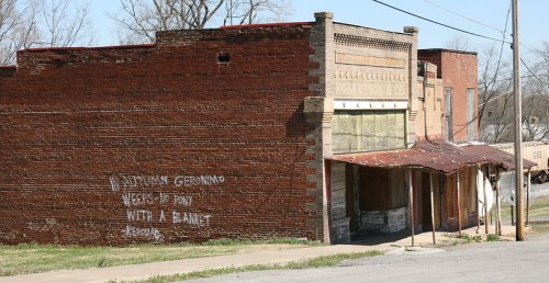 Abandoned brick building with a weathered facade and graffiti, set against a clear sky.