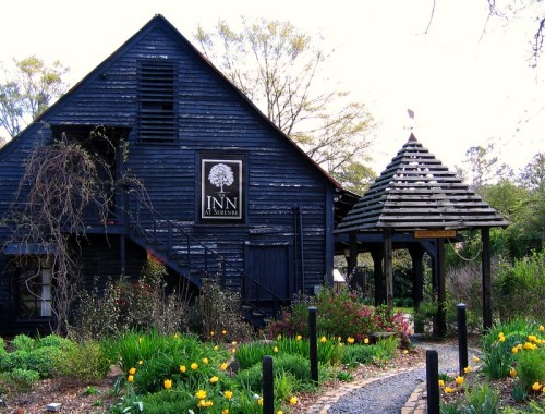 A charming black wooden inn with a gazebo, surrounded by colorful flowers and greenery.