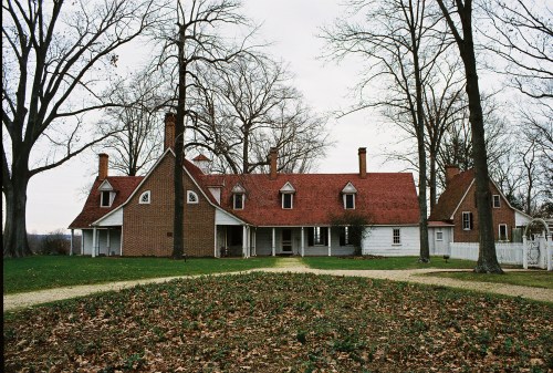 A large, historic house with a red roof, surrounded by trees and a grassy area covered in fallen leaves.