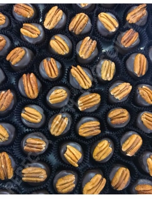 A close-up of chocolate-covered candies topped with pecans, arranged neatly in a black tray.
