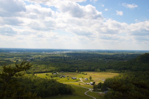 A panoramic view of lush green fields and rolling hills under a partly cloudy sky.
