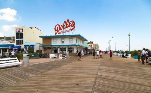 A wooden boardwalk with people walking, featuring a building with a large sign that reads "Dolle's."