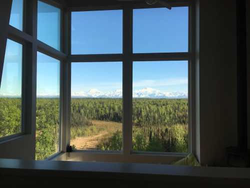 A scenic view from a window showcasing mountains and lush greenery under a clear blue sky.