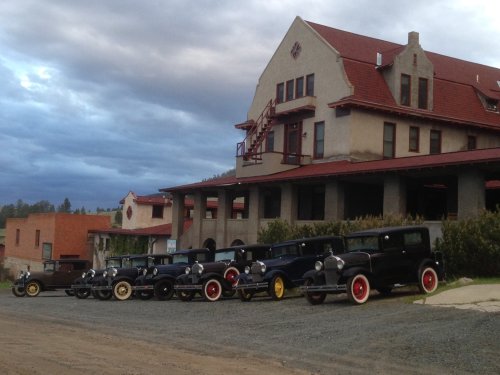 A row of vintage cars parked in front of a historic building under a cloudy sky.