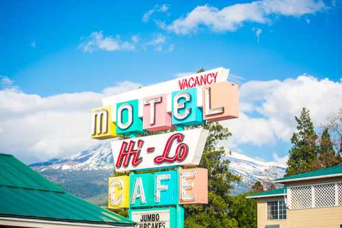 Colorful vintage sign for "Motel Hi-Lo Cafe" with a "Vacancy" notice against a backdrop of mountains and blue sky.