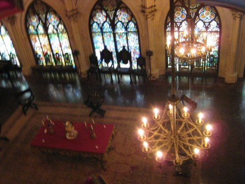 A grand interior with stained glass windows, a chandelier, and ornate furnishings in a historic setting.