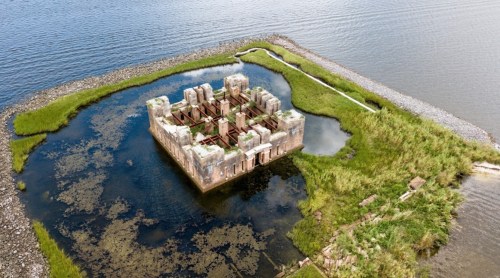 Aerial view of a partially submerged, overgrown stone structure surrounded by water and greenery.