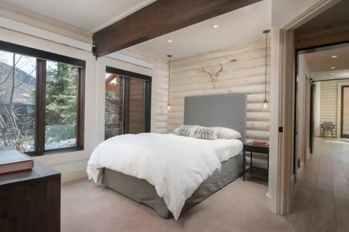 Cozy bedroom with a large bed, wooden accents, and windows overlooking greenery. Soft lighting creates a warm atmosphere.