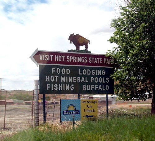 Sign for Hot Springs State Park featuring directions for food, lodging, fishing, and hot mineral pools, with a buffalo statue.