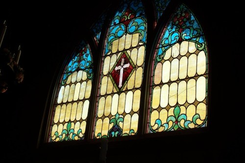 Stained glass window featuring a central cross, surrounded by colorful floral designs and geometric patterns.