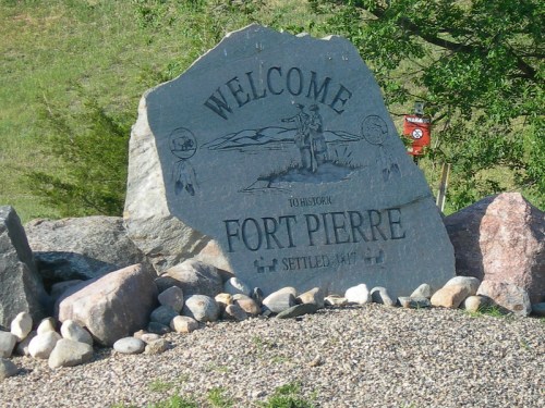 A large stone sign reading "Welcome to Historic Fort Pierre, Settled 1847," surrounded by pebbles and greenery.