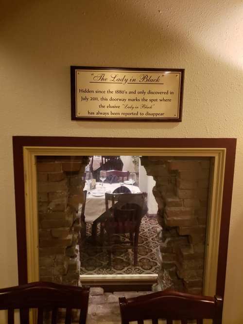 A sign reads "The Lady in Black" above a bricked-up doorway, leading to a dining area in a restaurant.