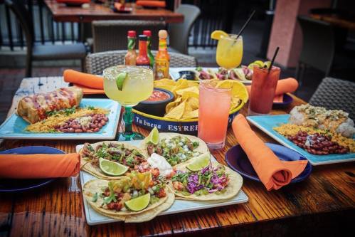 A vibrant table spread featuring tacos, burritos, chips, and colorful drinks, set in a lively dining atmosphere.
