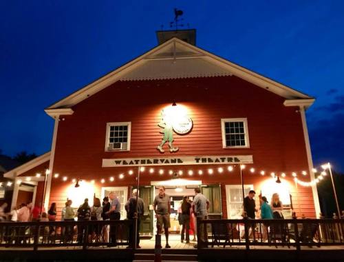 A vibrant red theater building at dusk, with people gathered outside under string lights.