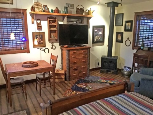Cozy interior of a cabin featuring a dining table, TV, wooden furniture, and a wood stove with decorative artwork.