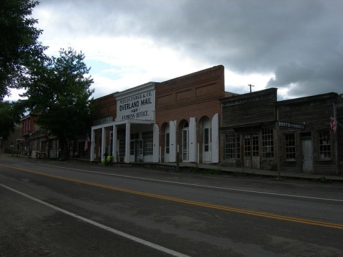 Historic buildings line a quiet street, featuring storefronts with vintage signage and a cloudy sky overhead.