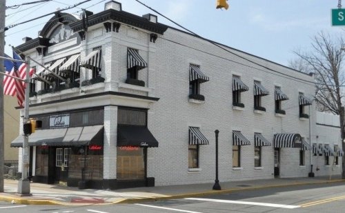 A white brick building with black and white striped awnings, featuring large windows and an American flag outside.