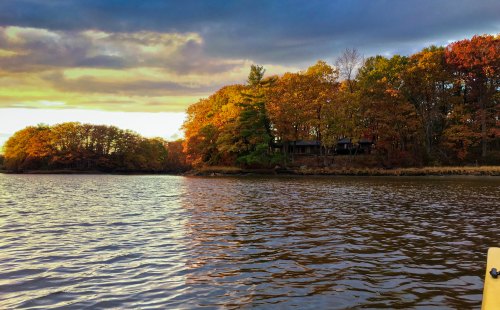 A serene lake scene with colorful autumn trees lining the shore under a cloudy sky.