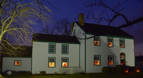 A white house with green trim, decorated for the holidays, illuminated windows, and a dark evening sky.