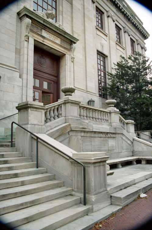 Stone steps lead up to a grand building entrance with ornate details and large windows.