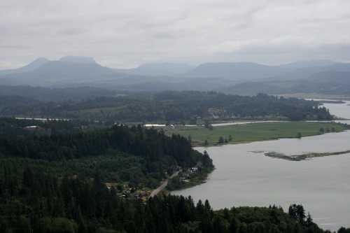 A scenic view of a river winding through lush green hills and mountains under a cloudy sky.