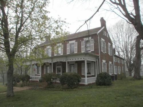A large, two-story brick house with a porch, surrounded by trees and greenery in a foggy setting.