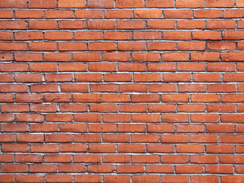 A close-up view of a textured red brick wall with a uniform pattern of bricks and mortar.