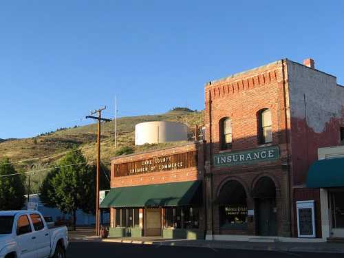 Historic buildings in a small town, with a water tower and mountains in the background under a clear blue sky.