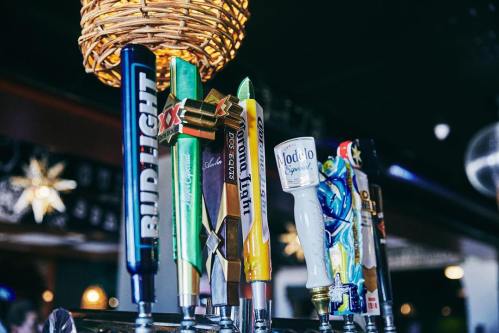 A row of colorful beer taps featuring various brands in a bar setting.