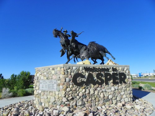 Bronze sculpture of horses and riders atop a stone base, welcoming visitors to Casper against a clear blue sky.