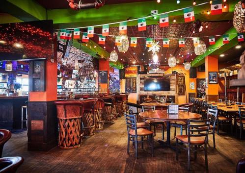 Colorful restaurant interior with festive decorations, including Mexican flags and vibrant lighting. Tables and bar area visible.