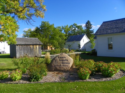 A stone monument honoring Laura Ingalls Wilder surrounded by greenery and buildings under a clear blue sky.