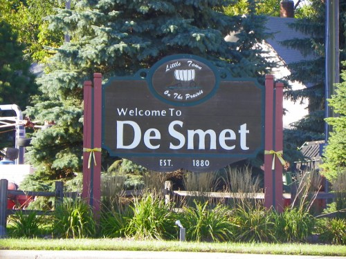 Welcome sign for De Smet, established in 1880, surrounded by greenery and trees.