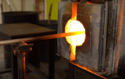 A glowing furnace with molten material, as a metal rod is inserted into the bright opening.