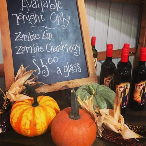 A chalkboard sign lists "Zombie Zin" and "Zombie Chardonnay" wines for $5 a glass, surrounded by decorative pumpkins.