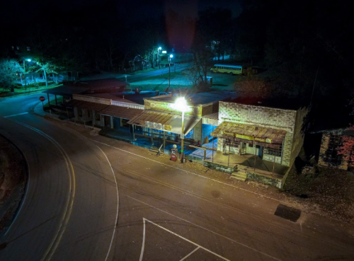A dimly lit, abandoned storefront at night, with a winding road and trees in the background.
