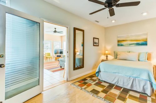 Cozy bedroom with a blue bedspread, a rug, and a doorway leading to a bright living area.
