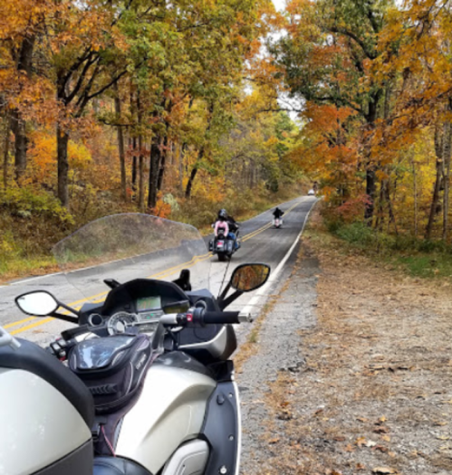 Two motorcycles on a winding road surrounded by colorful autumn trees.