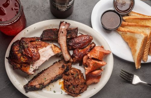 A platter of assorted barbecue meats including brisket, ribs, and chicken, served with toast and dipping sauces.