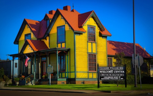 Bright yellow Victorian-style house with a red roof, featuring a sign for the Tennessee Williams Welcome Center.