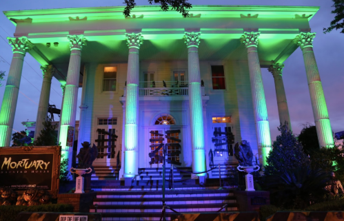 A large, illuminated mortuary building with green and blue lights, featuring tall columns and decorative statues.